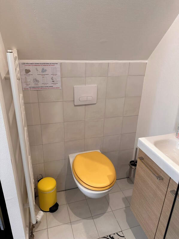A small bathroom with a toilet, a yellow trash bin, a hand dryer, and a cabinet. - Les Cigognes de Rosheim (Rosheim)