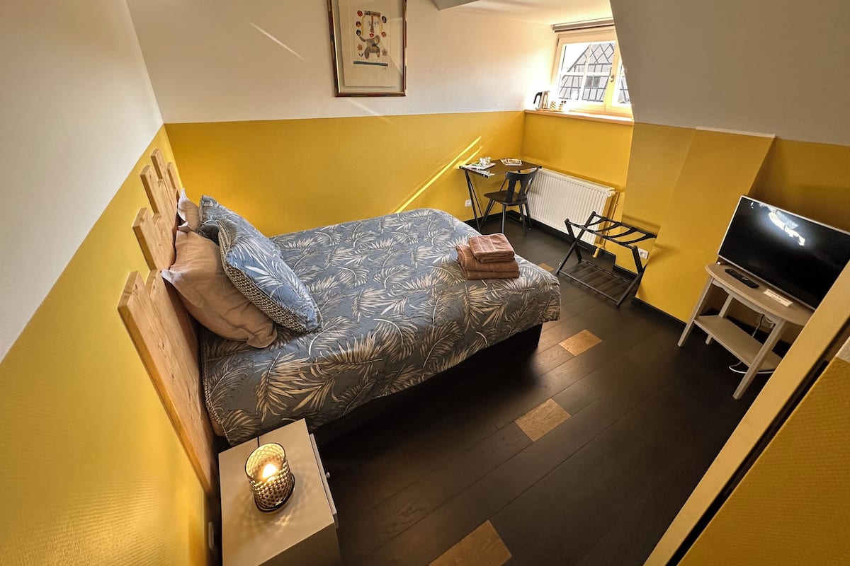 Une chambre à coucher de taille réduite, comprenant un lit, une télévision, une petite table et une fenêtre.