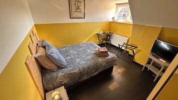 A compact bedroom with a bed, a TV, a small table, and a window.