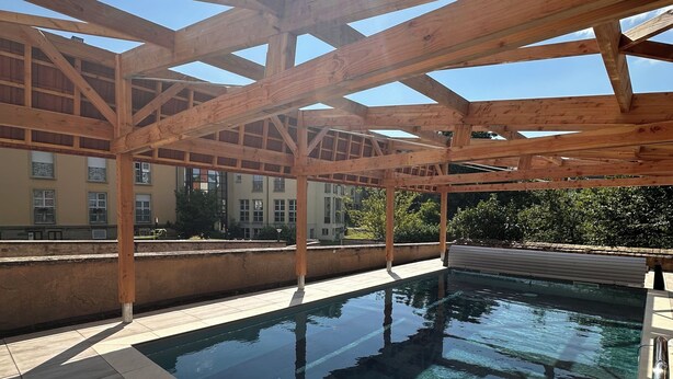Una piscina con un porche de madera sobre ella y un suelo de baldosas.