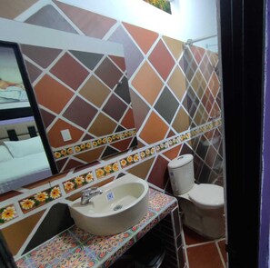 Un baño con lavamanos, inodoro y espejo. Las paredes están cubiertas de azulejos con un diseño geométrico.