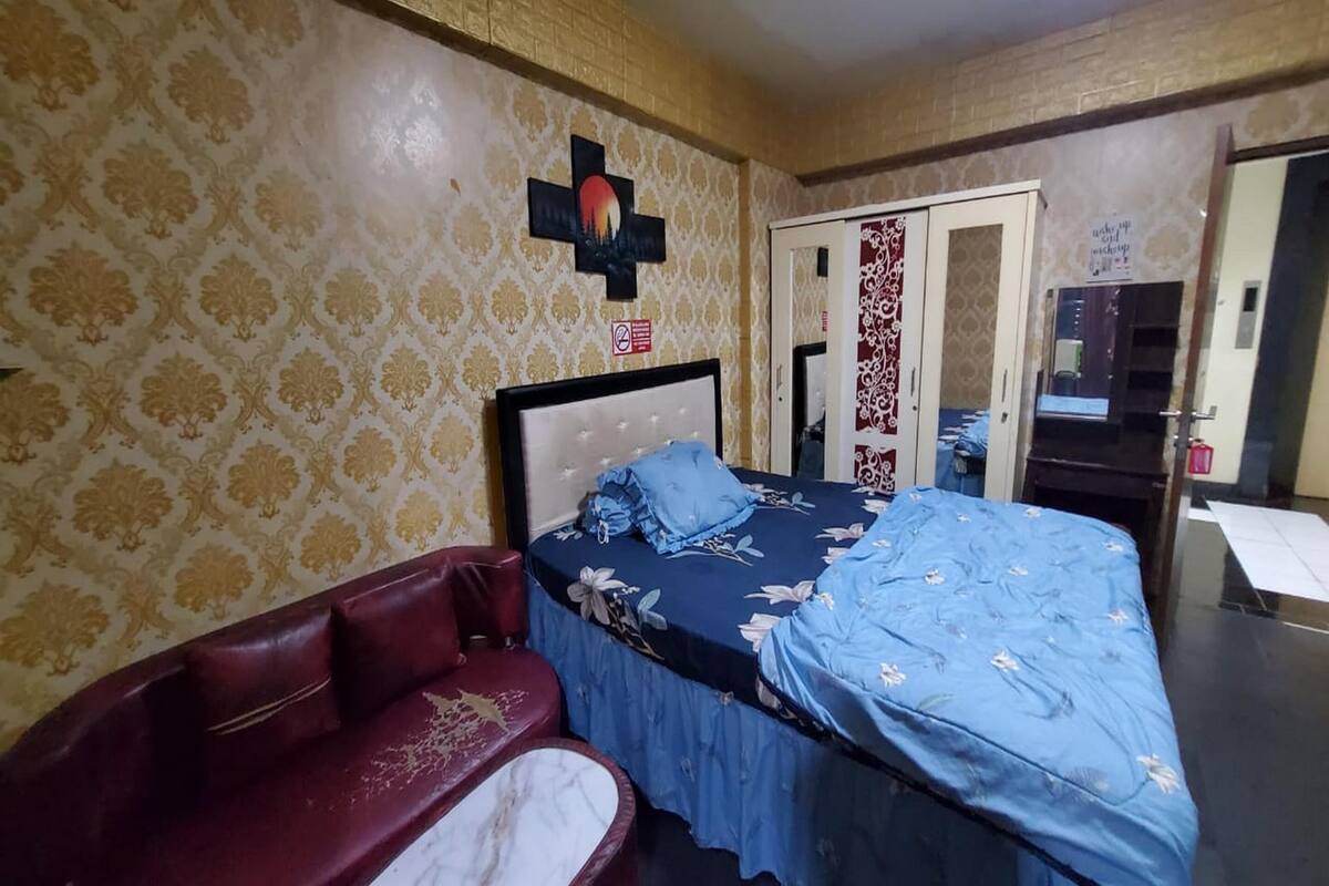 Une pièce comprenant un lit, un canapé en cuir rouge, un papier peint à motifs et une porte avec un miroir.