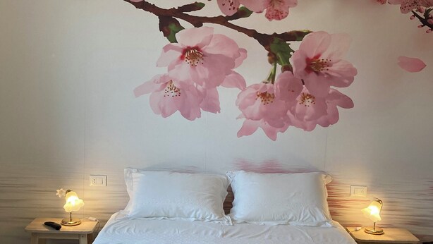 A bedroom with a bed, two bedside tables, and a wall mural of pink flowers. - RENTAL ROOMS "AT THE GRANDFATHER'S HOUSE" convenient, strategic and quiet site (Campodarsego)