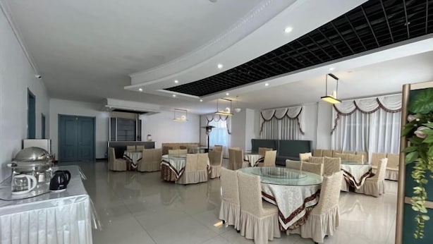 A modern dining area with round tables and cushioned chairs, a kitchen in the background, and a ceiling with a grid pattern. - Hailar Dongsheng Luxury Hotel (Hailar Airport Branch) (Hulunbuir)