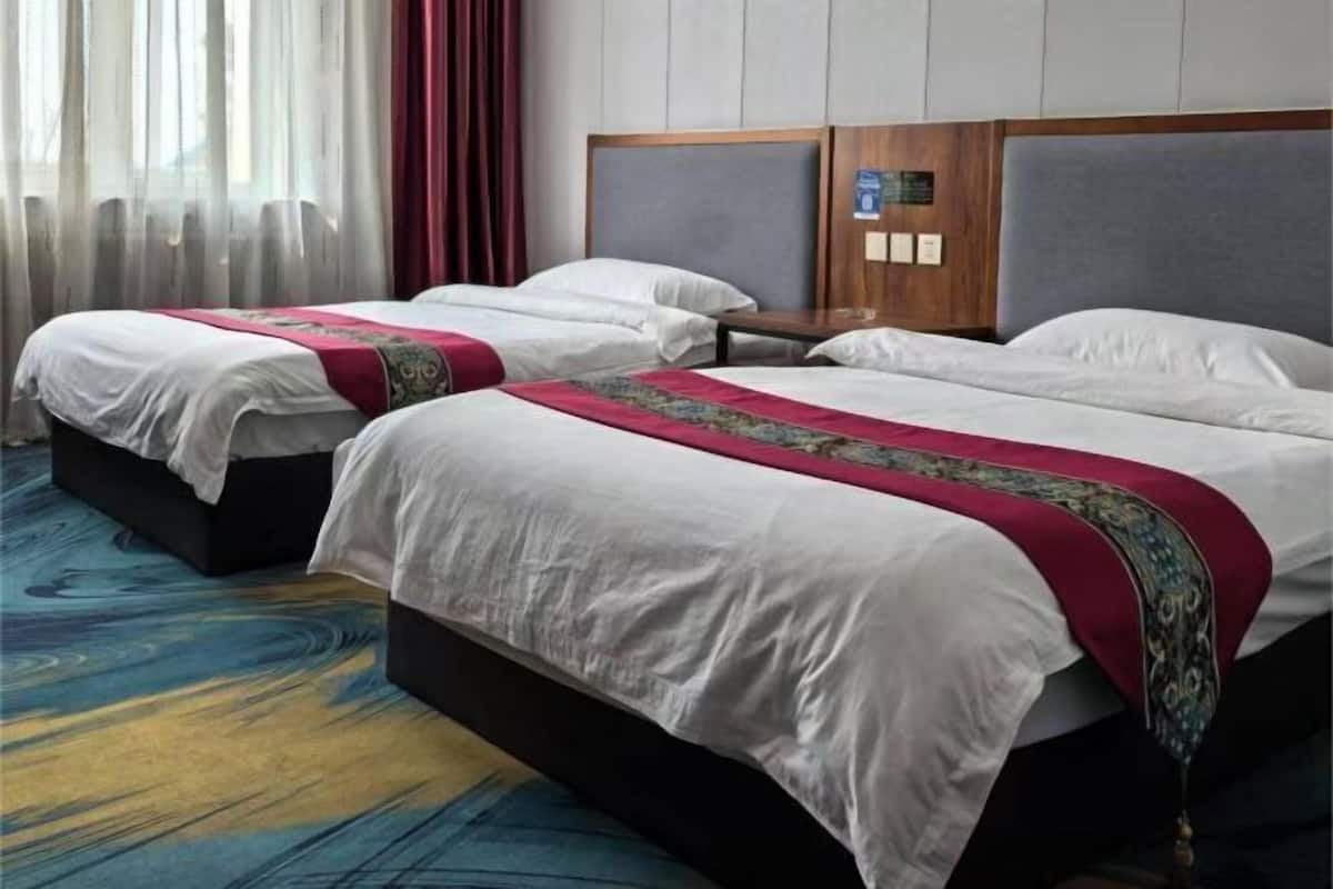 A hotel room with two beds, a wooden headboard, a nightstand, and a window with curtains.