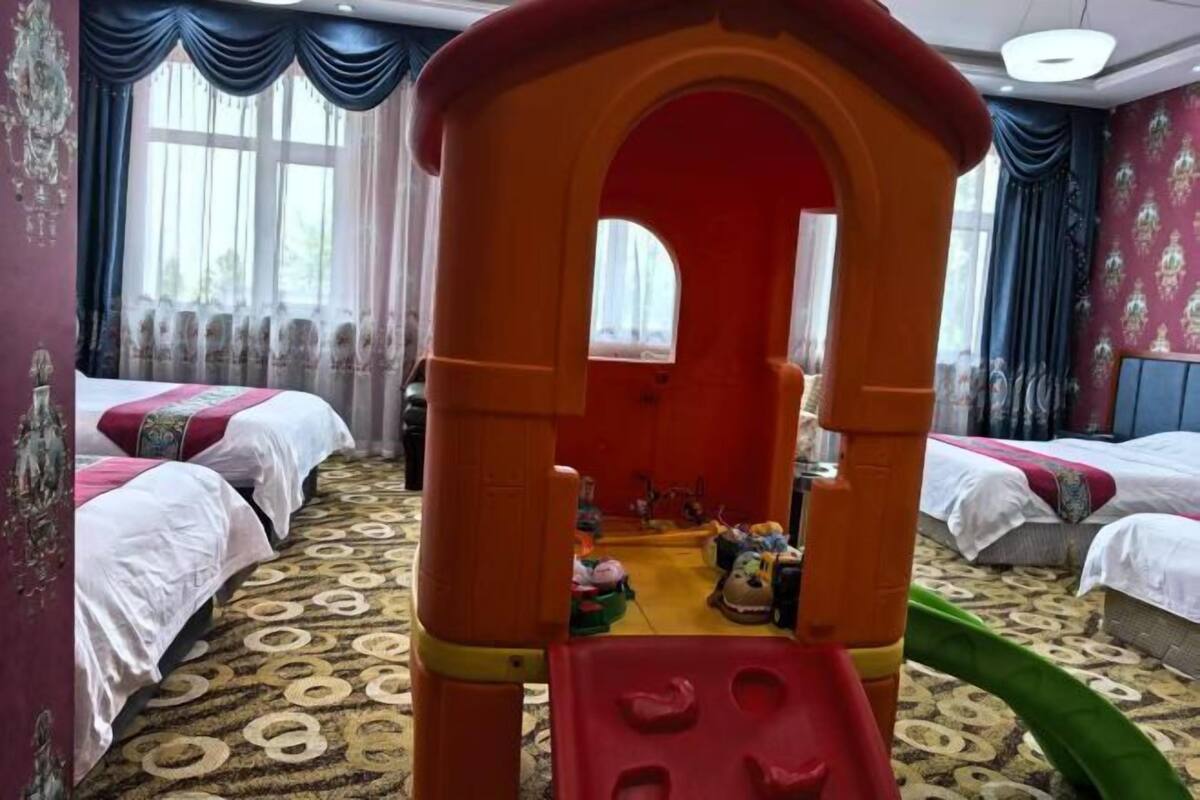 A hotel room with two beds, a play area, and a patterned carpet.