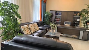A modern living room with a black leather sofa, a coffee table, and a reception desk. There are potted plants and a bookshelf in the background. - Hailar Dongsheng Luxury Hotel (Hailar Airport Branch) (Hulunbuir)