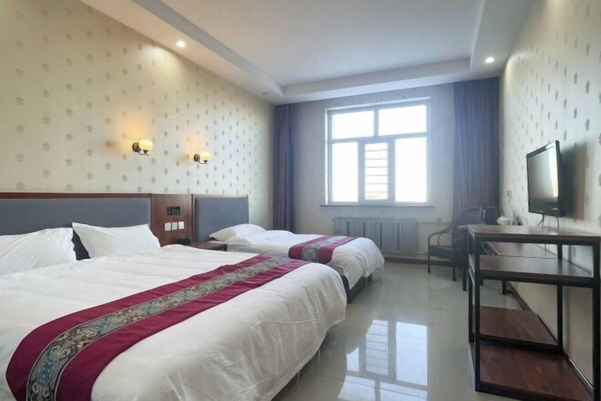 A hotel room with two beds, a desk, a chair, a television, and a window with curtains.