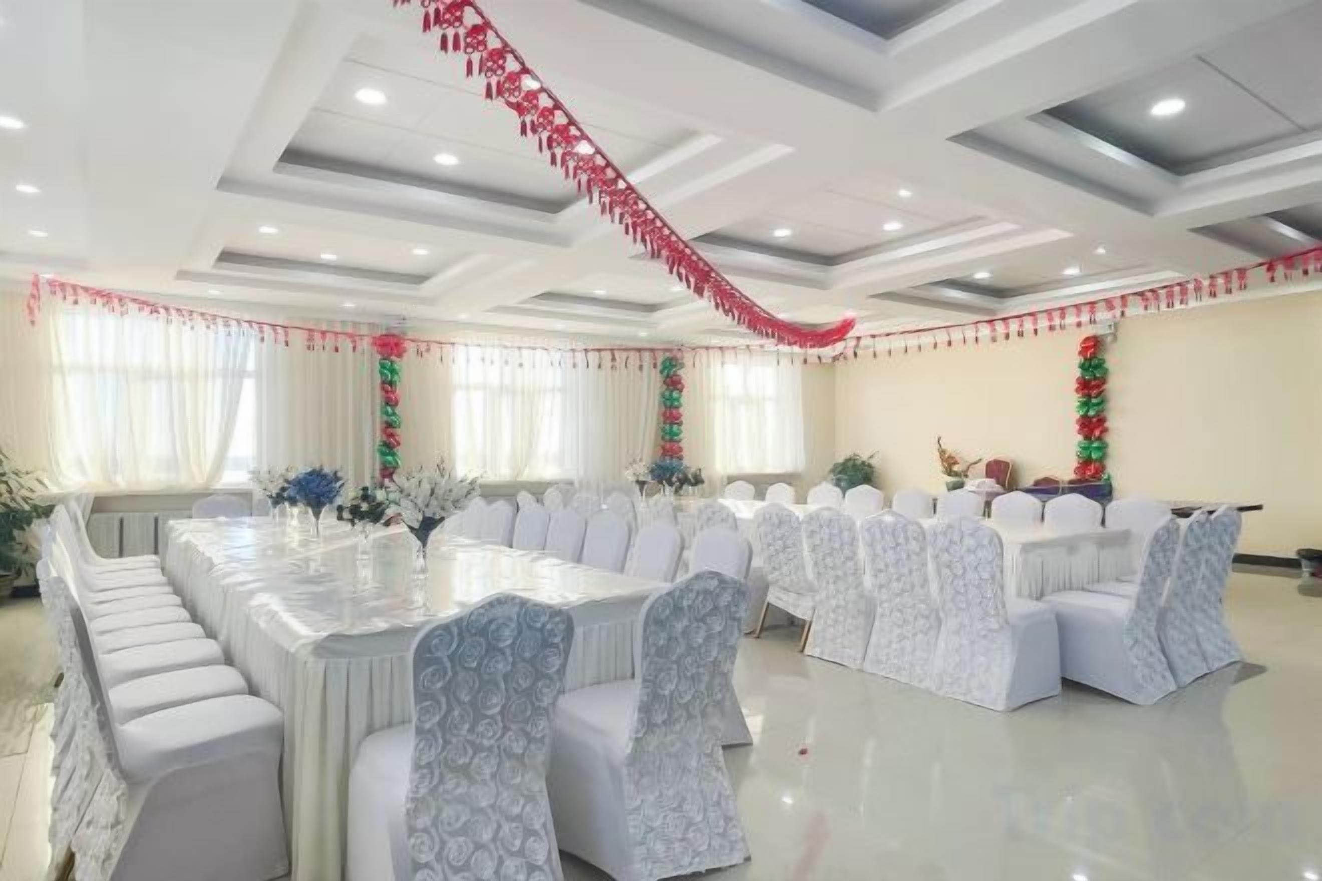 A banquet hall with a long table, white chairs, and red and green decorations.