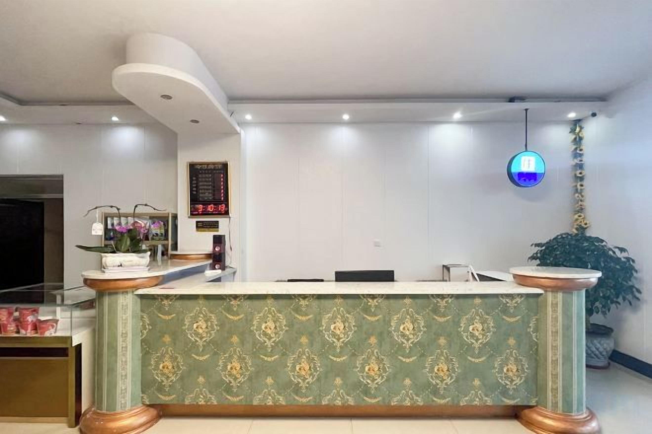 Un comptoir d'accueil avec un panneau décoratif à motifs, une horloge numérique et un luminaire suspendu.