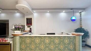 Un comptoir d'accueil avec un panneau décoratif à motifs, une horloge numérique et un luminaire suspendu.