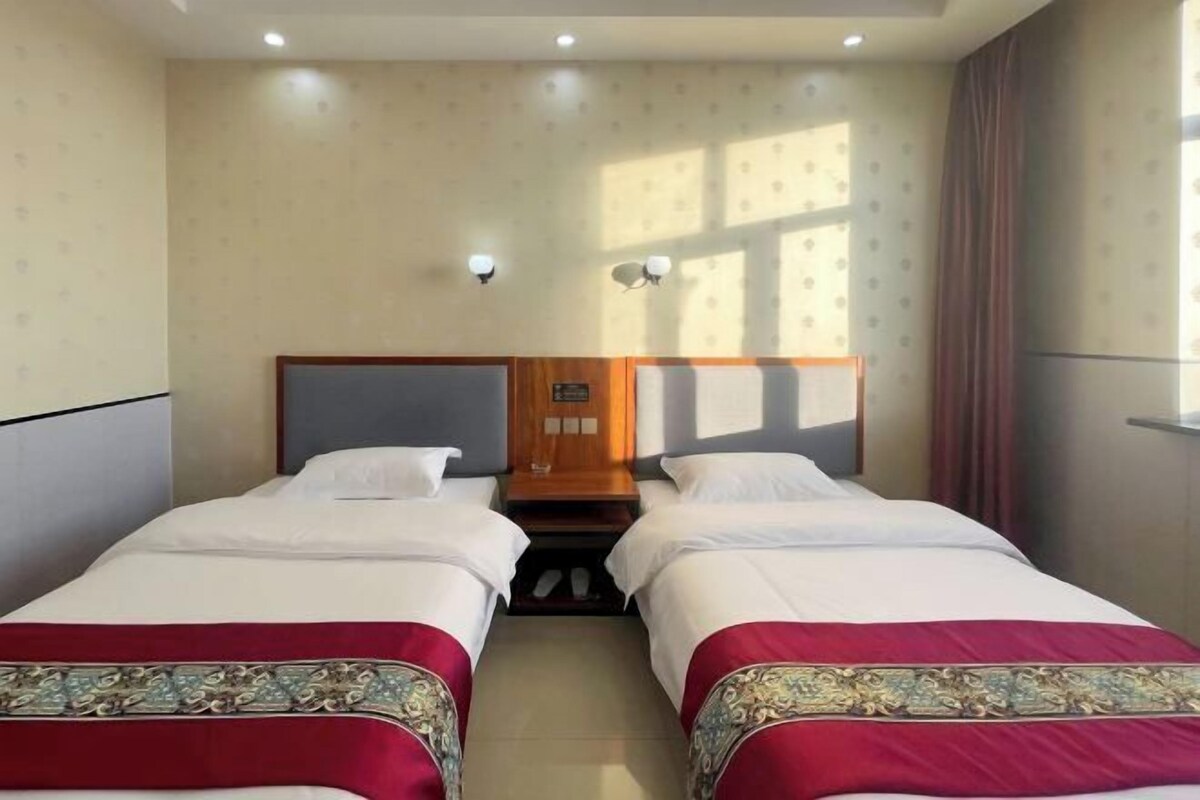 A hotel room with two beds, a wooden headboard, a nightstand, and a window with curtains.