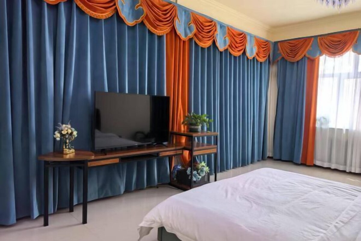 Un dormitorio con una cama, un televisor sobre un mueble, cortinas y una ventana.