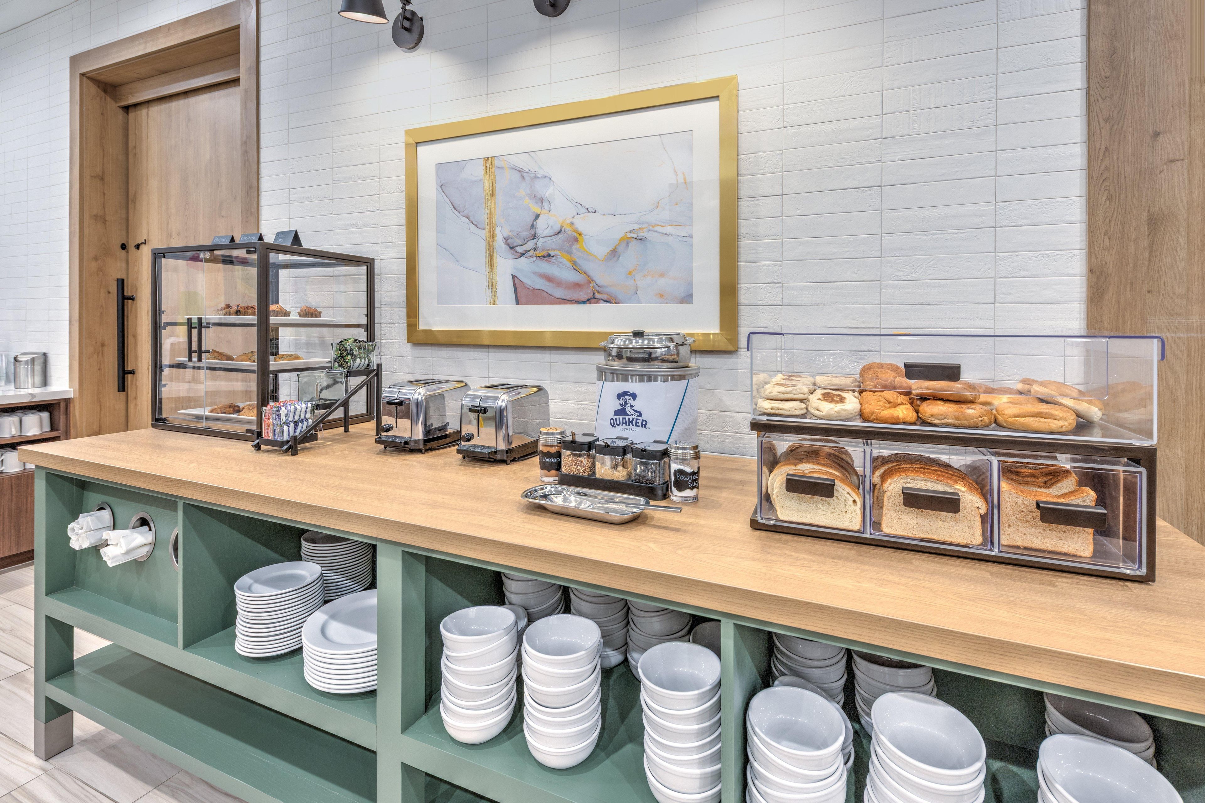 A breakfast buffet with various food items, a coffee machine, and a framed artwork on the wall.