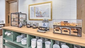 A breakfast buffet with various food items, a coffee machine, and a framed artwork on the wall.