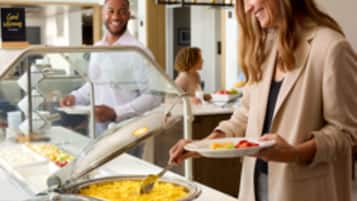 Een buffetgedeelte met diverse gerechten en iemand die eten opschept.