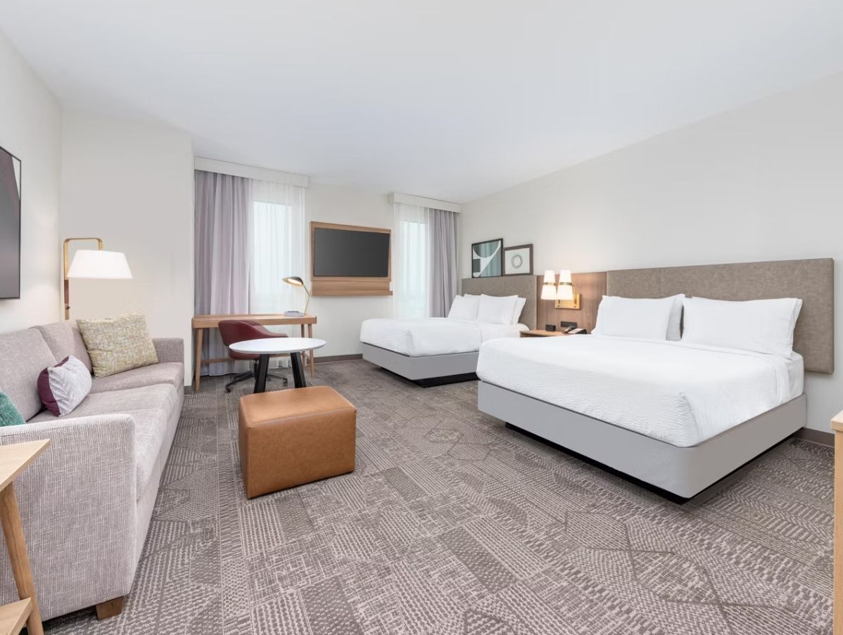 Ett hotellrum med en soffa, två enkelsängar, ett litet bord och en stol.