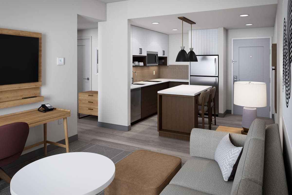 Una cocina moderna con una isla central, un comedor con una mesa redonda y una sala de estar con sofá y reposapiés.