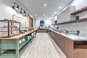 A modern kitchen with a marble countertop, wooden cabinets, and a display case with baked goods. - Staybridge Suites Port Arthur Mall Area (Port Arthur)