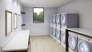 A laundry room with multiple washing machines, a wooden floor, a white countertop, and a window with a view of trees.