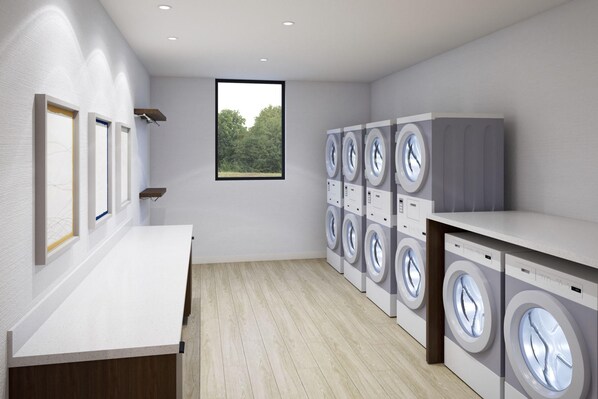 A laundry room with multiple washing machines, a wooden floor, a white countertop, and a window with a view of trees. - Staybridge Suites Port Arthur Mall Area (Port Arthur)
