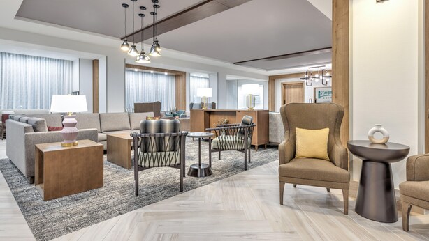A modern hotel lobby with a sofa, armchairs, a coffee table, and a dining area. - Staybridge Suites Port Arthur Mall Area (Port Arthur)