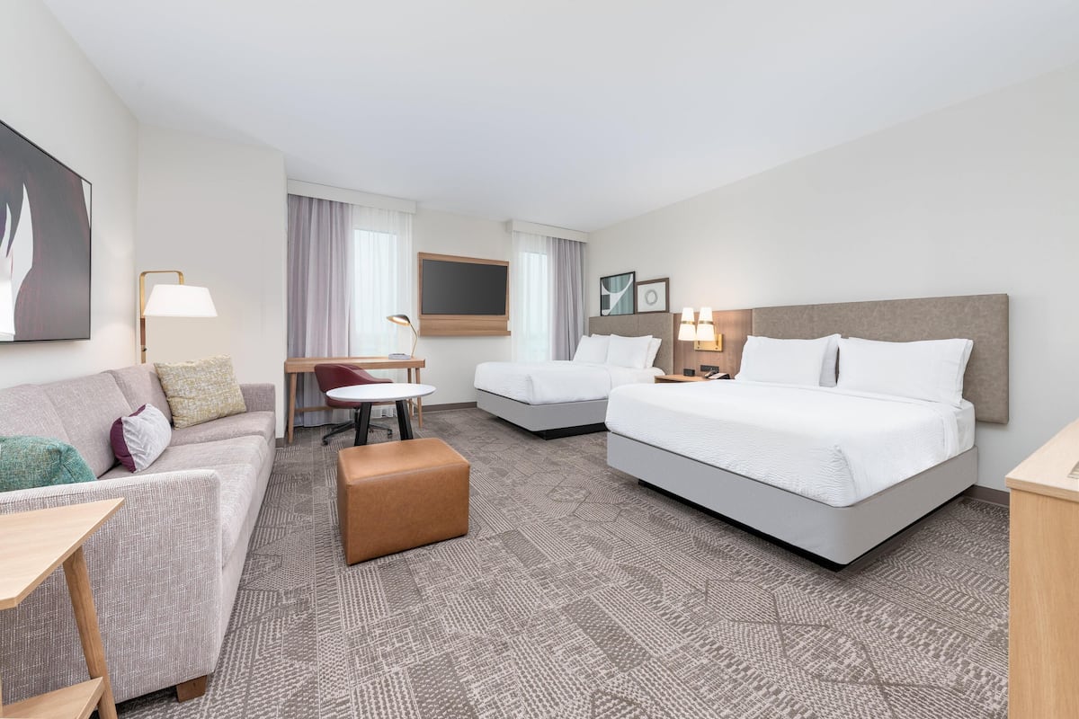 Una habitación de hotel con una cama grande, un sofá, una mesita y un escritorio.