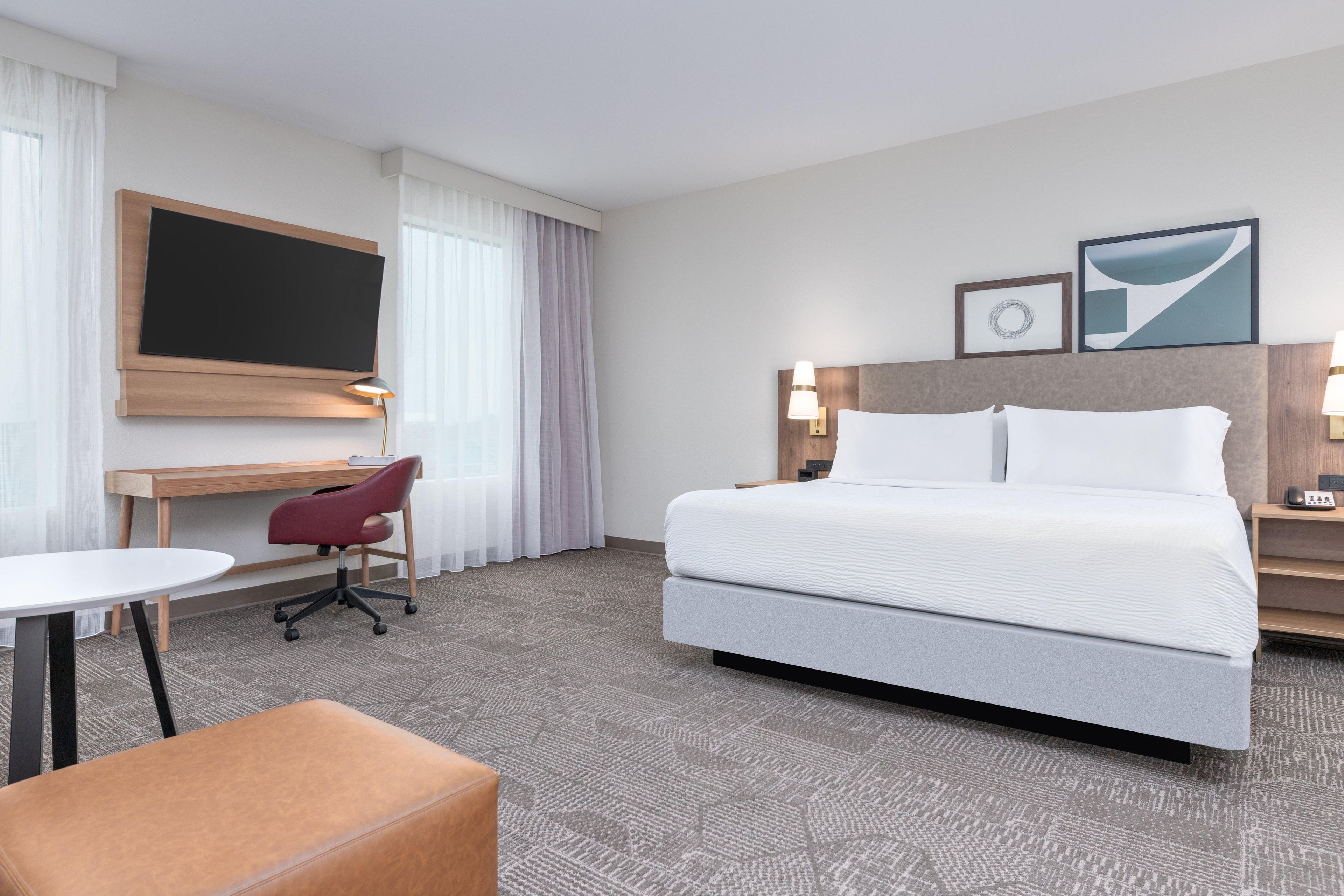 Een hotelkamer met een groot bed, een bureau met stoel, een aan de muur bevestigde televisie en twee bedlampjes.