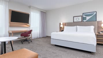 Een hotelkamer met een groot bed, een bureau met stoel, een aan de muur bevestigde televisie en twee bedlampjes.