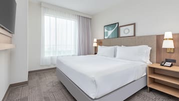 Een hotelkamer met een groot bed, twee nachtkastjes met lampen, een flatscreen televisie en een raam met gordijnen.