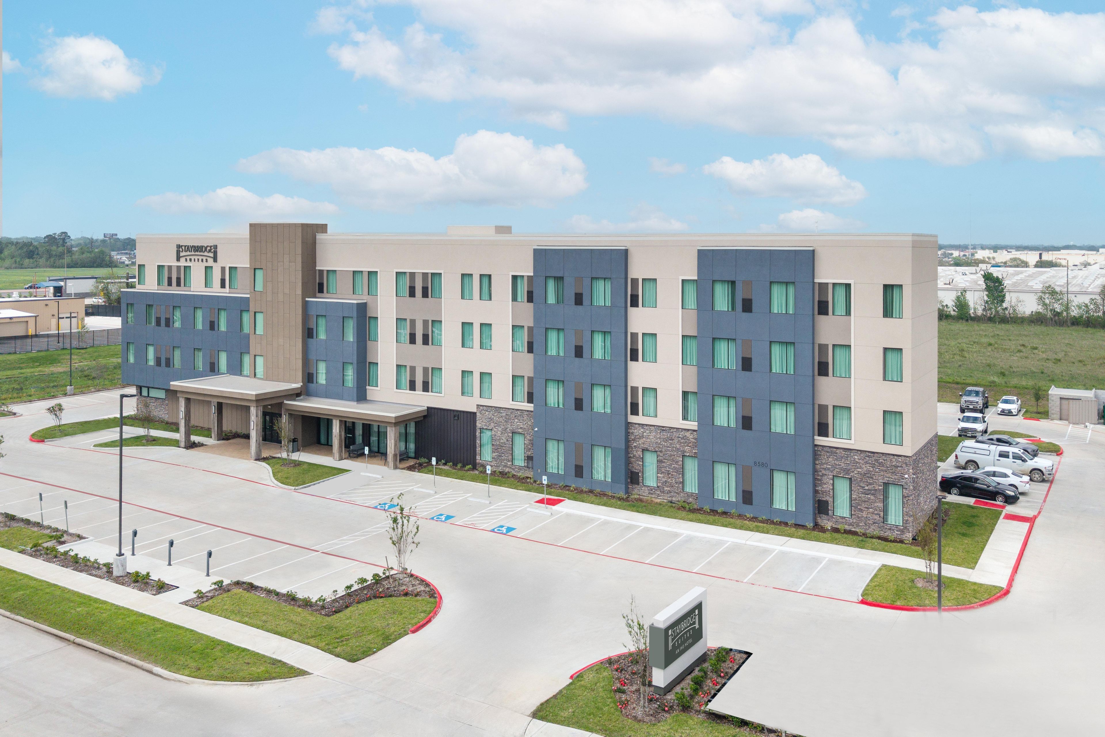 A multi-story hotel with a modern design, featuring a central entrance, a parking lot with marked handicapped spaces, and a clear view of the surrounding area.