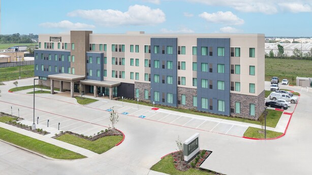 A multi-story hotel with a modern design, featuring a central entrance, a parking lot with marked handicapped spaces, and a clear view of the surrounding area.