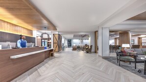 A modern hotel lobby with a wooden reception desk, a herringbone-patterned floor, and a seating area with sofas and a coffee table. - Staybridge Suites Port Arthur Mall Area (Port Arthur)
