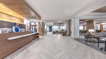 En modern hotellobby med en receptionsdisk i trä, ett golv med fiskbensmönster och en sittgrupp med soffor och ett soffbord.