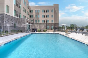 A swimming pool with a clear blue water, surrounded by a black fence, and a building with multiple windows and a stone facade. - Staybridge Suites Port Arthur Mall Area (Port Arthur)