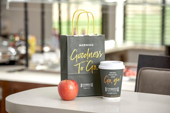 A coffee cup and a black bag with gold text on a table. - Staybridge Suites Port Arthur Mall Area (Port Arthur)