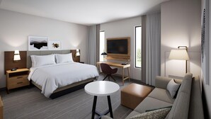 A modern hotel room with a bed, desk, chair, sofa, and a TV. - Staybridge Suites Port Arthur Mall Area (Port Arthur)