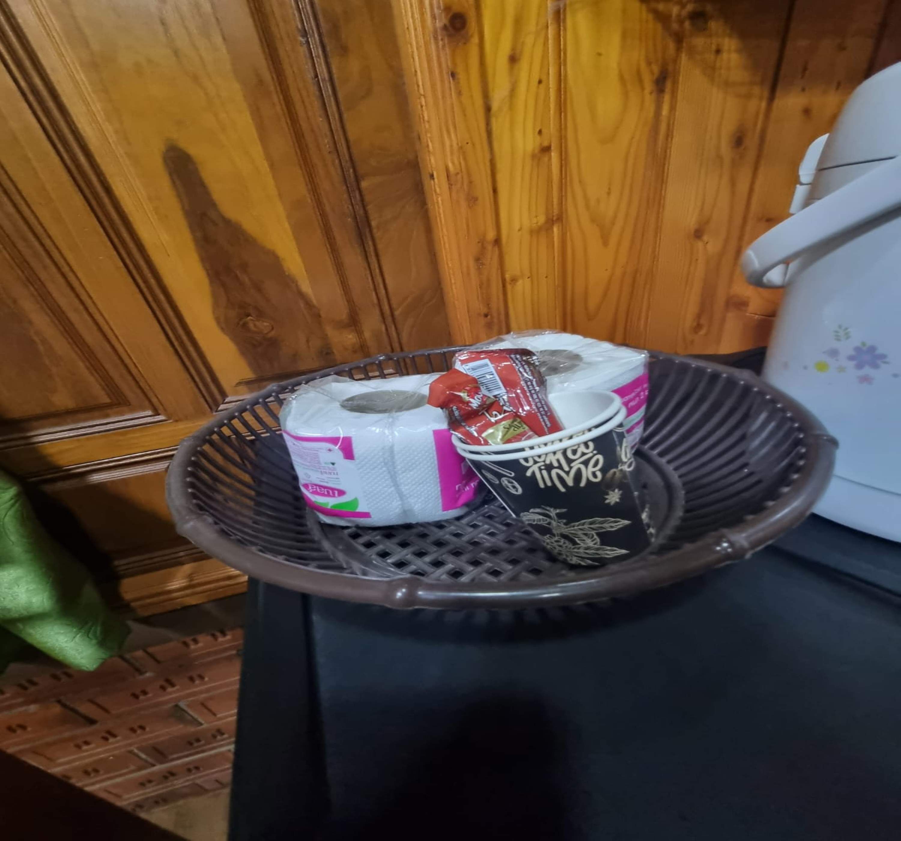 A basket containing paper towels, a coffee mug, and a box of tissues on a table.