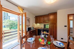 Uma área de refeições com uma mesa posta para dois, uma cesta de frutas e vista para o exterior.
