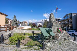 Un monumento con un cannone, circondato da un muro di pietra e una catena, in una piazza pubblica con edifici sullo sfondo.