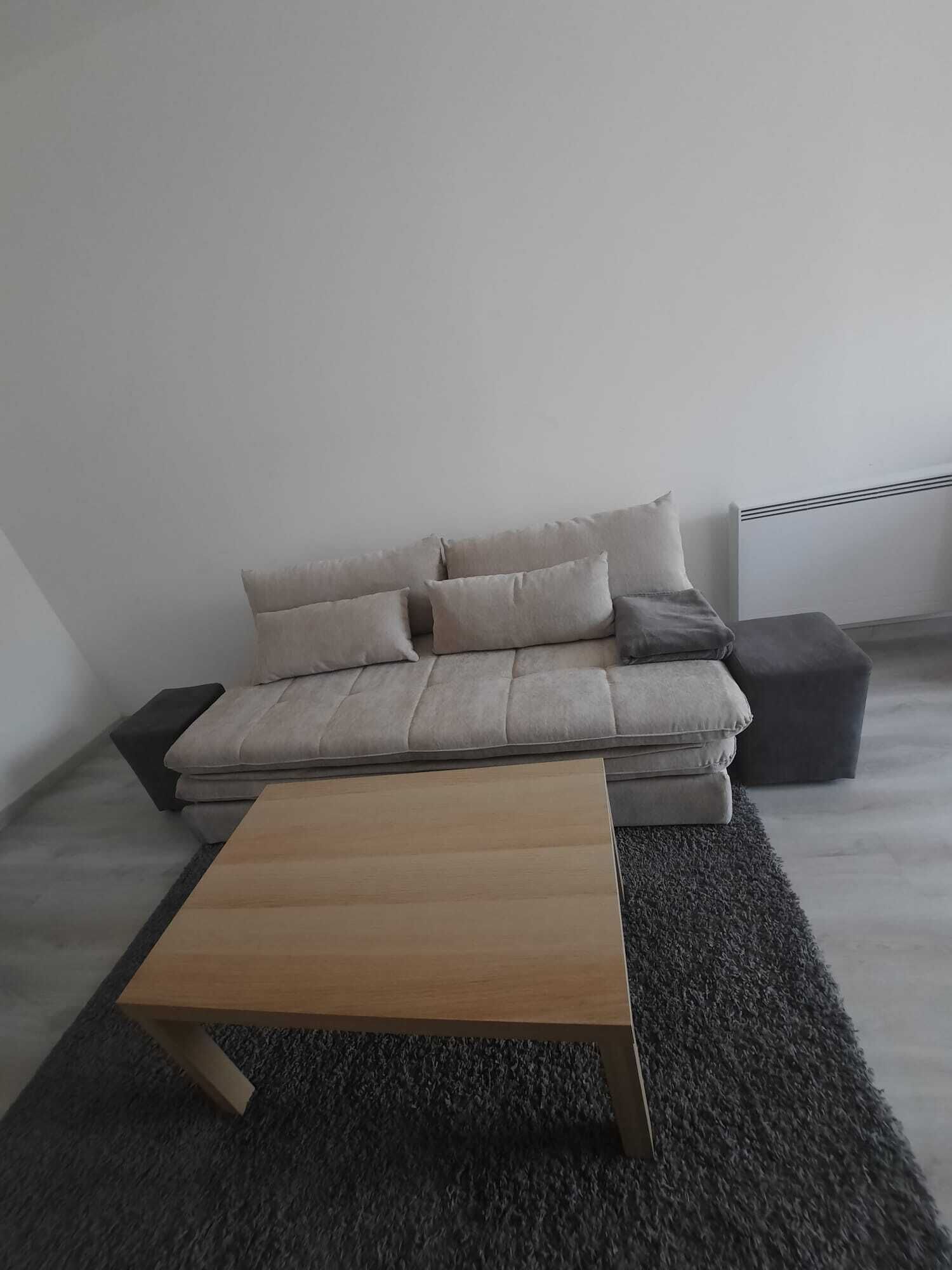 Ein modernes Wohnzimmer mit einem grauen Sofa, einem Holztisch und einem dunkelgrauen Teppich.