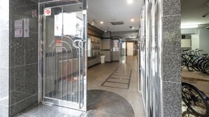 A modern building entrance with a glass door, a tiled floor, and a bicycle parking area to the right. - Dotonbori East Residence Haru (Osaka)