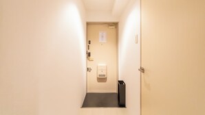 A narrow hallway with a door at the end, a hand sanitizer dispenser, and a trash bin. - Dotonbori East Residence Haru (Osaka)