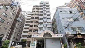 A multi-story building with a central entrance, air conditioning units, and a vending machine outside. - Dotonbori East Residence Haru (Osaka)