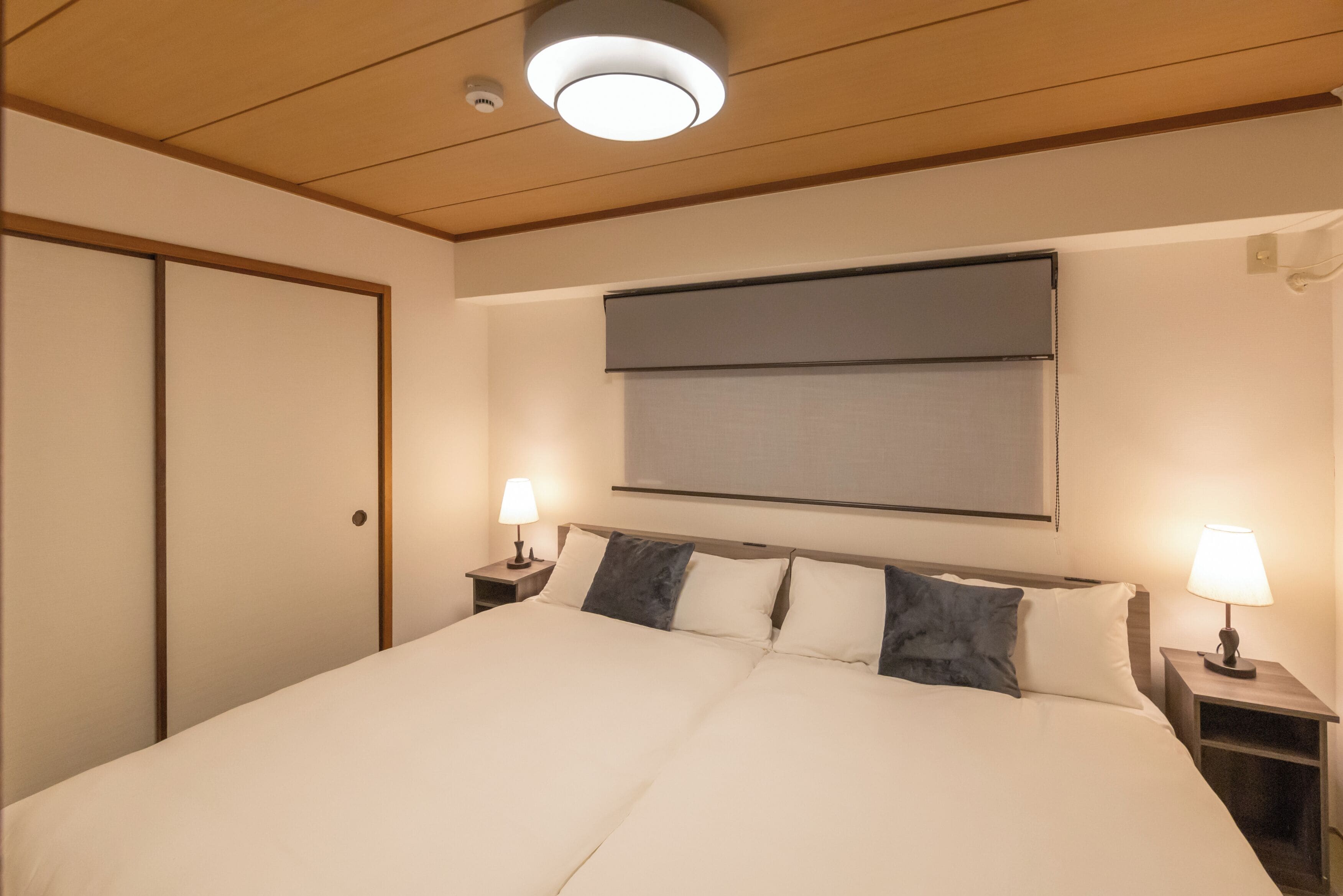 Une chambre d’hôtel avec un grand lit, deux tables de chevet avec des lampes, un luminaire au plafond et une porte coulissante.