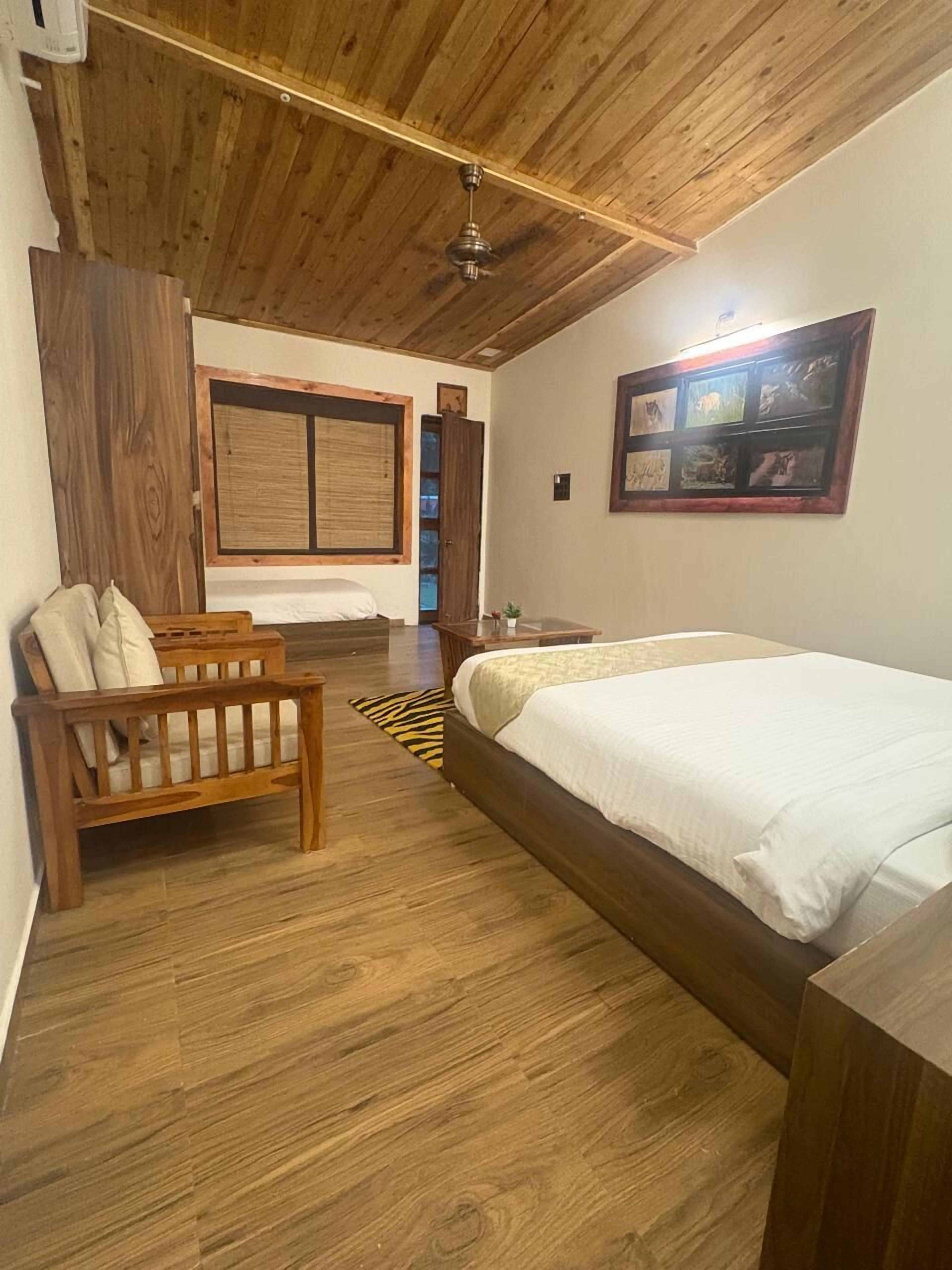 Un dormitorio con techo de madera, una cama, un banco de madera, una ventana con persianas y un cuadro en la pared.
