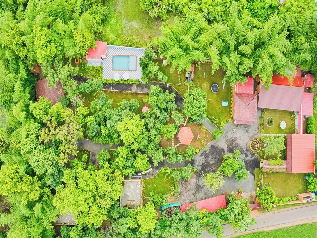 An aerial view of a residential area with a swimming pool, multiple houses, and a small water body.