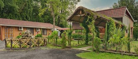 A hotel with a gravel driveway, a wooden fence, and a thatched-roof structure.