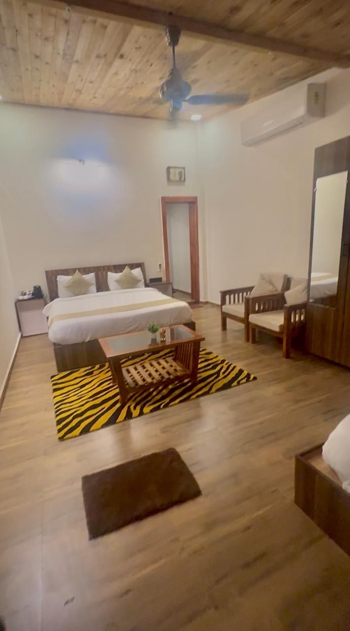 A hotel room with a wooden ceiling, a bed with white linens, a wooden nightstand, a wooden chair, a small table, and a zebra-patterned rug.
