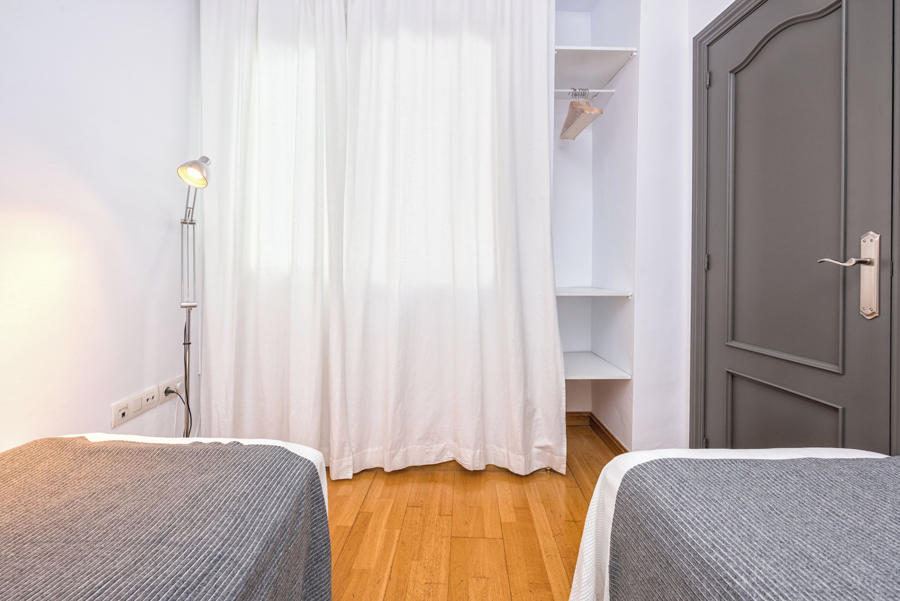 A room with two beds, a wardrobe, a closet with hanging clothes, and a door.